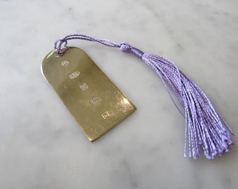 May include: A silver bookmark with a purple tassel. The bookmark is rectangular with rounded corners and has several hallmarks on the front.