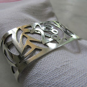 Peut inclure: Bague à serviette en argent avec un motif décoratif découpé. Le motif présente un motif répétitif de cercles et de lignes.