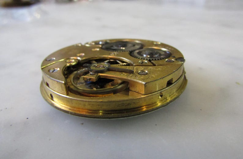 May include: Close-up of a gold-toned pocket watch movement with intricate gears and a winding mechanism.