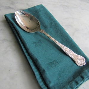May include: A silver spoon with an ornate handle sits on a folded teal green napkin.