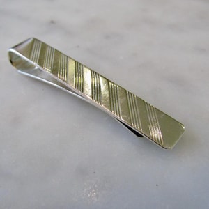 May include: A silver tie bar with a striped pattern.