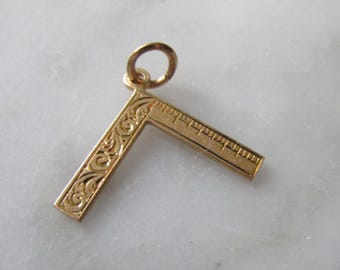 May include: Gold-toned charm in the shape of a carpenter's square with an ornate design and a ruler on the longer side.
