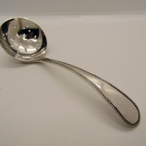 May include: A silver sugar spoon with a perforated bowl and a beaded handle.