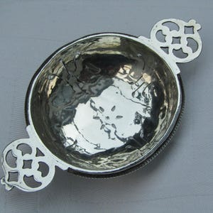 Peut inclure: Un bol argenté avec une texture martelée et des poignées décoratives. Le bol est rond avec un bord détaillé et deux poignées ajourées ornées. L'intérieur reflète la lumière, donnant un aspect métallique brillant. Un article de cuisine décoratif.