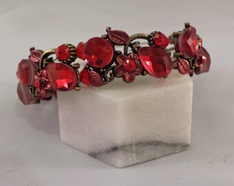 May include: A red and gold jeweled bracelet with a floral design. The bracelet is made of metal and has a variety of red gemstones.
