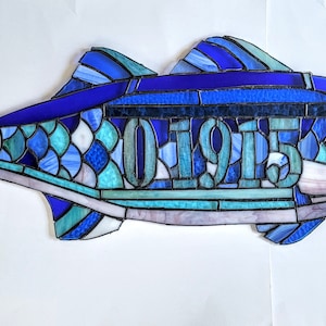 Puede incluir: Un pez de vidrio azul con el número 01915 en el centro.