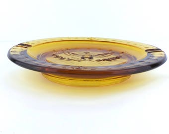 May include: Amber glass ashtray with a raised design of an eagle with outstretched wings and a banner that reads "United States of America".