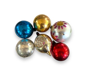 May include: A collection of vintage Christmas ornaments in various colors, including blue, gold, silver, and red. Some ornaments have decorative patterns, such as a pink floral design. The ornaments are round and teardrop-shaped.