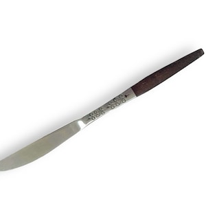 Puede incluir: Un cuchillo de mantequilla de plata con mango de madera marrón. El cuchillo tiene un patrón decorativo en el mango.