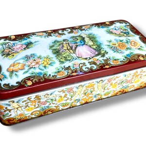 Peut inclure: Une boîte en étain rectangulaire vintage avec un couvercle rouge et une base blanche. Le couvercle présente un motif floral coloré avec un couple au centre. La base a un motif répétitif de chérubins et de fleurs.
