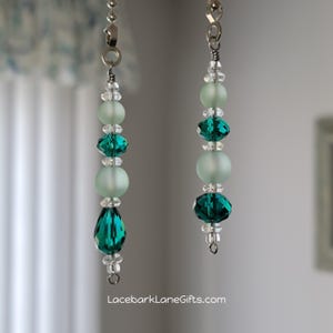 May include: Two beaded ceiling fan pull chains. Each chain features a combination of clear, teal, and frosted beads. The larger chain has a teardrop-shaped bead at the bottom. The website LacebarkLaneGifts.com is visible at the bottom.
