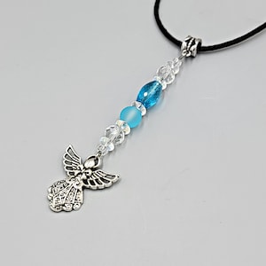 May include: A silver-toned angel pendant with a black cord necklace. The pendant features a detailed angel figure and is adorned with clear and blue beads. The beads include a frosted blue bead and a faceted blue bead. The necklace is suitable for everyday wear.