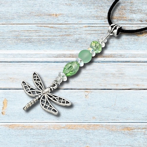 May include: A silver dragonfly pendant necklace with a black cord. The pendant features a detailed dragonfly design. The necklace includes green and clear beads.