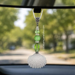 May include: A hanging car ornament featuring a white seashell at the base, topped with a vertical arrangement of green glass beads and a silver-toned metal connector. A white cord suspends the piece, which includes the text LacebarkLaneGifts.com.