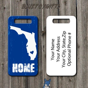 May include: A blue and white luggage tag with the outline of the state of Florida and the word "HOME" in white. The tag has a white area for personalization with the text "Your Name", "Your Address", "Your City, State, Zip", and "Optional Phone #".