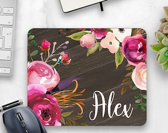 May include: A personalized mouse pad with a floral design. The background is a dark wood grain with a pink, white, and green floral pattern. The name "Alex" is written in white cursive lettering.