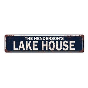 May include: Rustic blue and brown metal sign with white text that reads "The Henderson's Lake House".