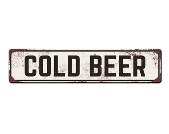 May include: A white metal sign with a distressed, rusty look. The sign reads "COLD BEER" in black letters.
