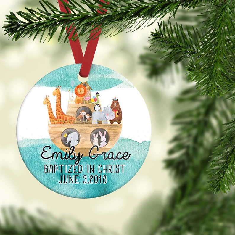 May include: A round, blue and white Christmas ornament with a watercolor illustration of a wooden ark filled with animals. The text "Emily Grace Baptized in Christ June 3, 2018" is written below the ark.