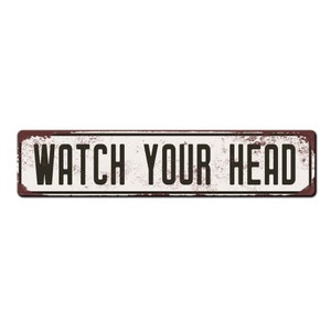May include: A rusty metal sign with white paint and black text that reads "WATCH YOUR HEAD".