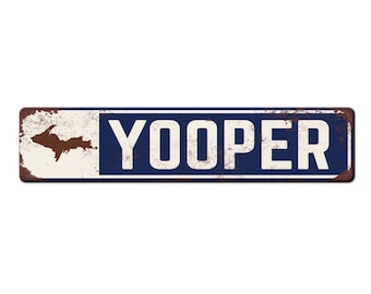 Puede incluir: Un letrero de metal oxidado con fondo blanco y letras azules. El letrero dice "YOOPER" y presenta un contorno marrón de la península superior de Michigan.