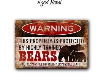 May include: A rustic metal sign with a warning sign that reads "WARNING" in red. The sign says "This property is protected by highly trained bears. Not responsible for injury or possible death." The sign has a distressed, aged metal look and features a silhouette of two bears.