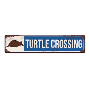 May include: A blue and white metal sign with the text "TURTLE CROSSING" in white letters. A brown silhouette of a turtle is on the left side of the sign.