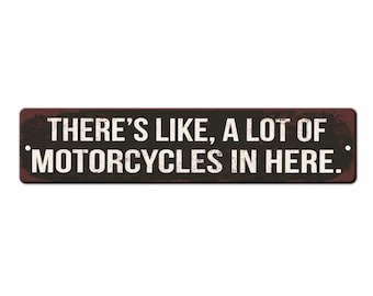 以下が含まれることがあります： 黒い背景に白い文字で「THERE'S LIKE, A LOT OF MOTORCYCLES IN HERE.」と書かれた、素朴な金属製の看板です。