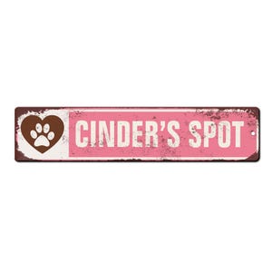May include: A pink and brown metal sign with the text "CINDER'S SPOT" and a brown heart with a white paw print inside.