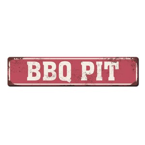 Pode incluir: Uma placa de metal vermelha com o texto "BBQ PIT" em letras brancas. A placa tem um visual desgastado e vintage.