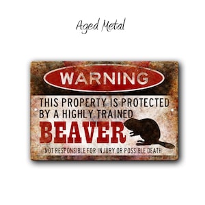May include: A rustic metal sign with a warning sign that reads "WARNING" in red letters. The sign says "This property is protected by a highly trained beaver. Not responsible for injury or possible death." The sign has a distressed, aged look.