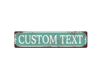 以下が含まれることがあります： 白い大文字で「CUSTOM TEXT」と書かれた長方形の金属製の看板。看板は、ターコイズブルーの背景と錆びた茶色のボーダーがあり、ヴィンテージ感があります。