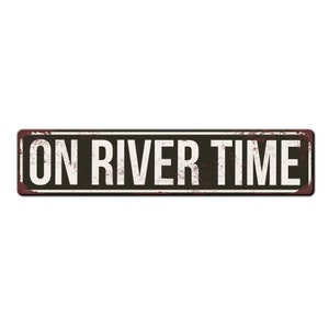 May include: A black and white metal sign with a rusty texture. The sign reads "ON RIVER TIME" in white letters.