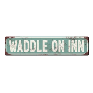 May include: A vintage-style metal sign with a rustic, weathered look. The sign is painted in a light blue color with a white border and the text "WADDLE ON INN" in white letters.