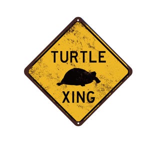 May include: Yellow diamond-shaped road sign with black text and a silhouette of a turtle. The sign reads "TURTLE XING".