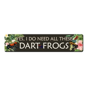 May include: A black and green sign with the text "YES, I DO NEED ALL THESE DART FROGS" in white. The sign is decorated with colorful frogs and tropical plants.