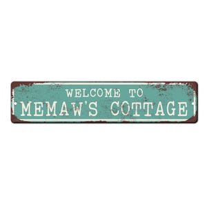 May include: A rustic metal sign with a teal background and brown edges. The sign reads "Welcome to Memaw's Cottage" in white lettering.
