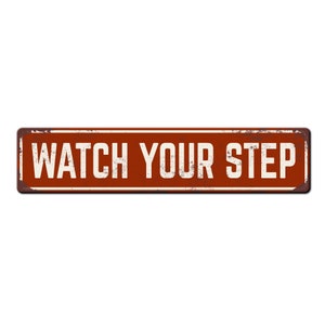 May include: A rusty red metal sign with white text that reads "WATCH YOUR STEP".