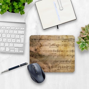 May include: A vintage-style mouse pad with a faded sheet music design. The music notes are printed in black ink on a beige background with brown and white accents. The text "Te l' Serrez un peu" is printed at the top of the mouse pad.