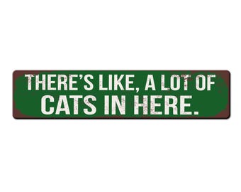 May include: A green and brown metal sign with the text "THERE'S LIKE, A LOT OF CATS IN HERE."