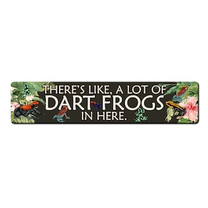 May include: A black and green sign with the text "There's like, a lot of dart frogs in here."  The sign is decorated with colorful dart frogs and tropical plants.