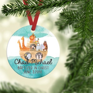 May include: A round, blue and white Christmas ornament with a watercolor design of Noah's Ark with animals. The ornament has the text "Chad Michael Baptized in Christ June 3, 2018".