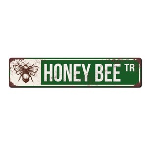 May include: A green and white metal sign with a rusty texture. The sign reads "Honey Bee Tr" and features a brown and white illustration of a bee.