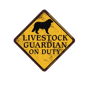 May include: Yellow diamond-shaped sign with black text and a silhouette of a dog. The sign reads "Livestock Guardian On Duty".
