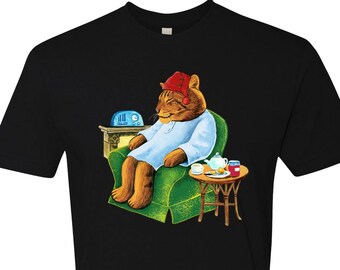 May include: A black t-shirt with a graphic of a cat wearing a red nightcap and pajamas, sitting in a green armchair with a cup of tea and a plate of cookies on a small table beside it.