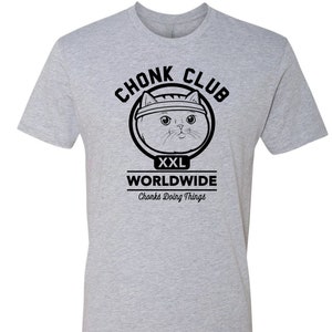 以下が含まれることがあります： 黒のヘッドバンドをした猫のグラフィックと「Chonk Club XXL Worldwide Chonk's Doing Things.」というテキストが書かれたグレーのTシャツです