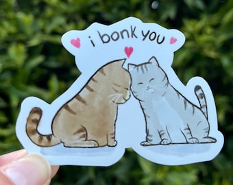 Può includere: Un adesivo bianco con due gatti dei cartoni animati, uno marrone e uno grigio, con il testo "i bonk you" e cuori rosa sopra.