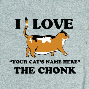 May include: A grey t-shirt with a black and white illustration of a calico cat. The text "I LOVE "YOUR CAT'S NAME HERE" THE CHONK" is printed on the shirt.