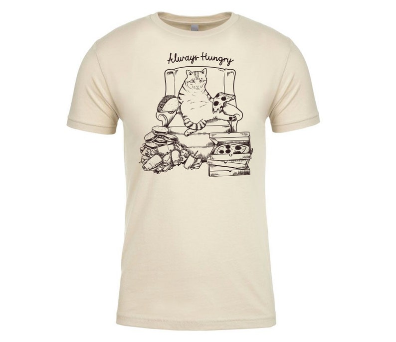 May include: A beige t-shirt with a black and white illustration of a cat sitting in a chair with pizza and other food around it. The text "Always Hungry" is above the cat.