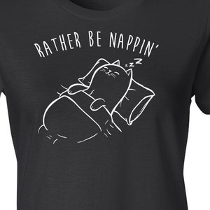 Puede incluir: Camiseta negra con un gráfico blanco de un gato durmiendo en la cama con el texto "Rather Be Nappin'" sobre el gato.